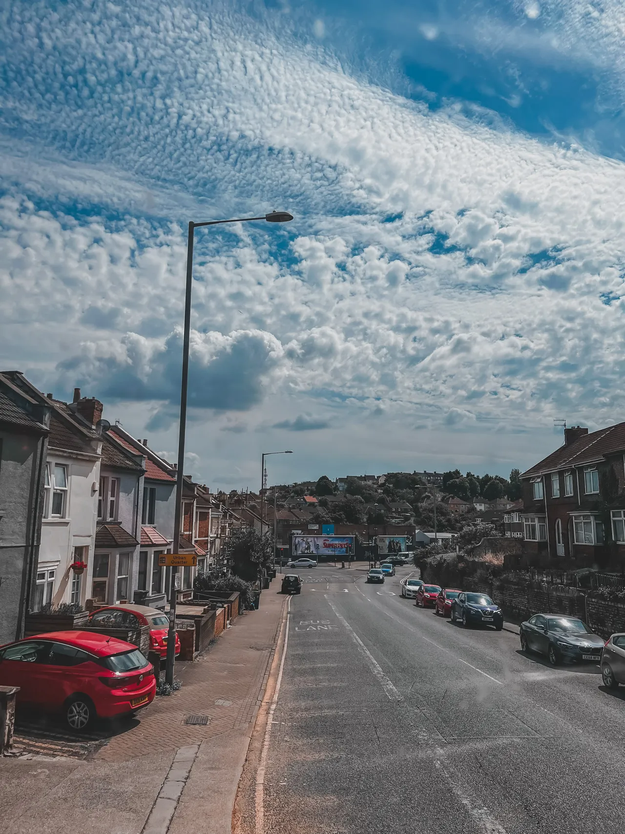 A long residential street runs downhill towards the town under a wide sky of rippled cloud.