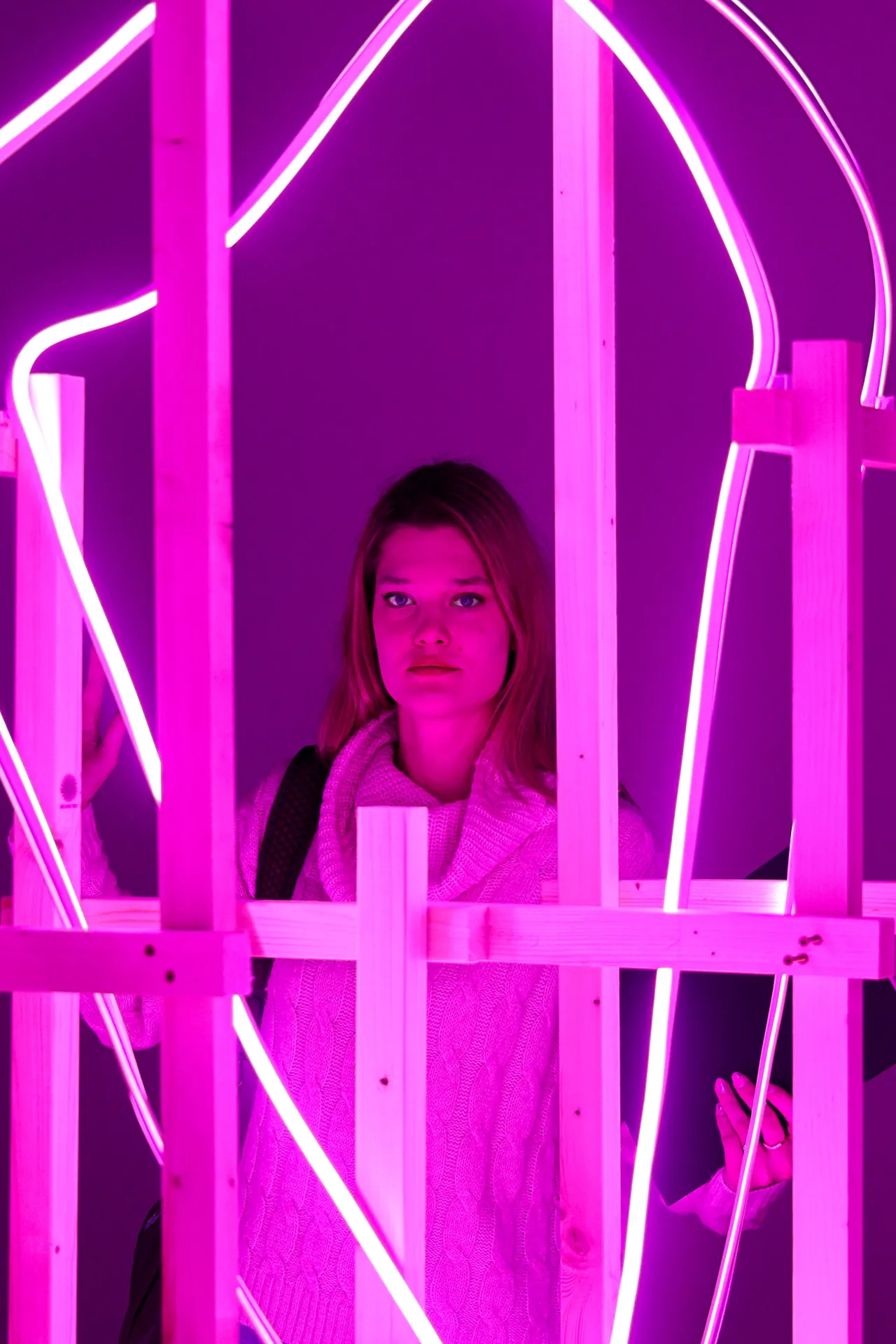 A figure framed inside a glowing magenta light sculpture, face half-lit in pink.