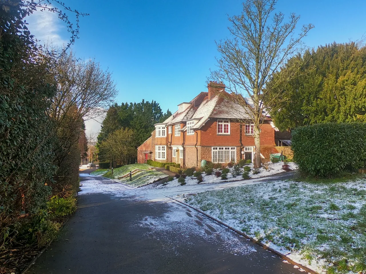 A red-brick house at the end of a lane, a light dusting of snow on the grass beneath a clear blue sky.