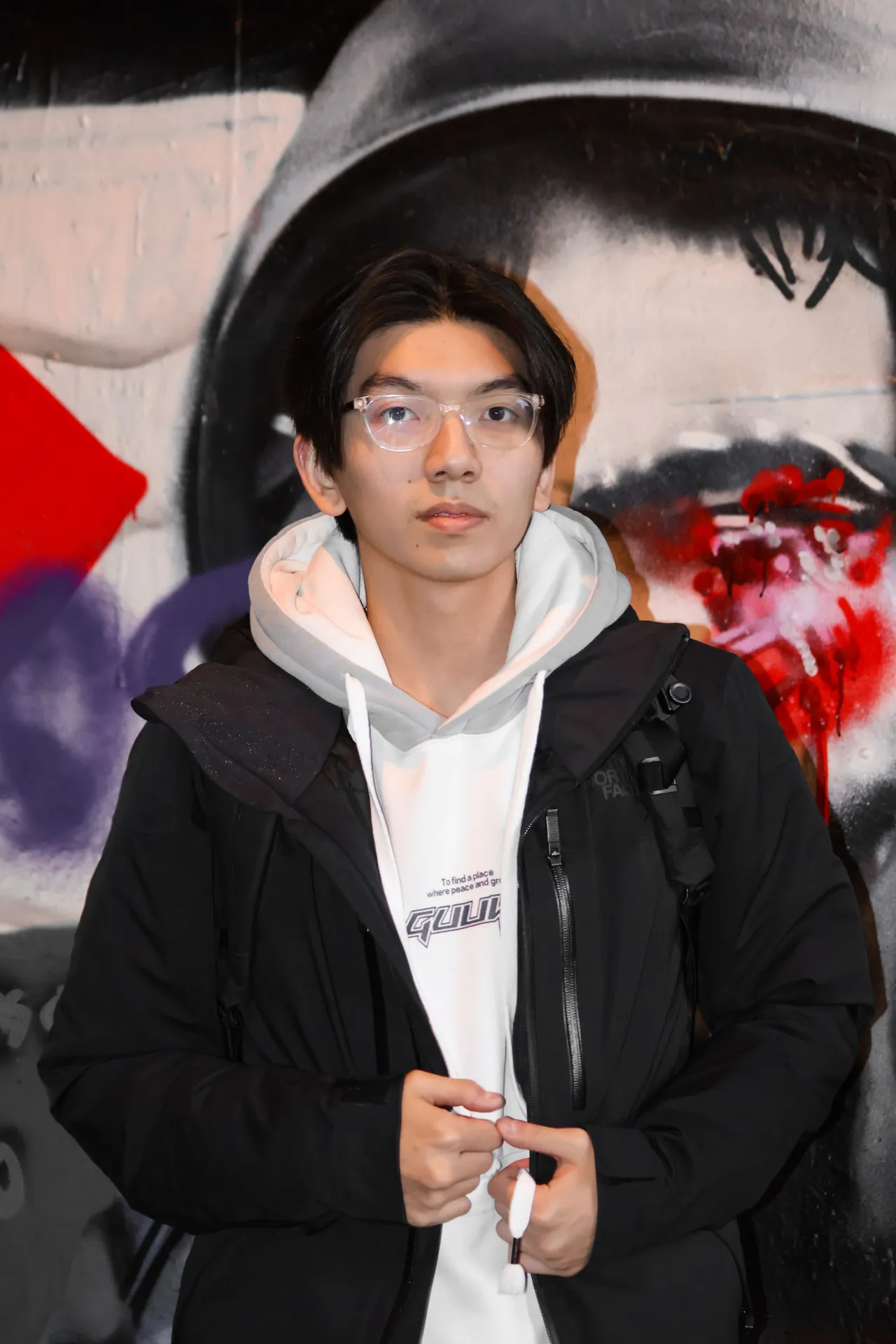 Wilson Zhao in a white hoodie and black jacket, standing in front of a graffiti mural.